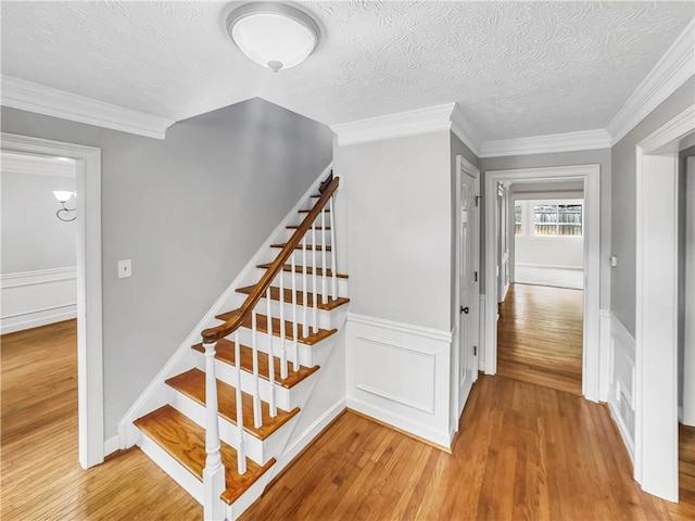 stairs featuring hardwood / wood-style flooring, crown molding, and a textured ceiling