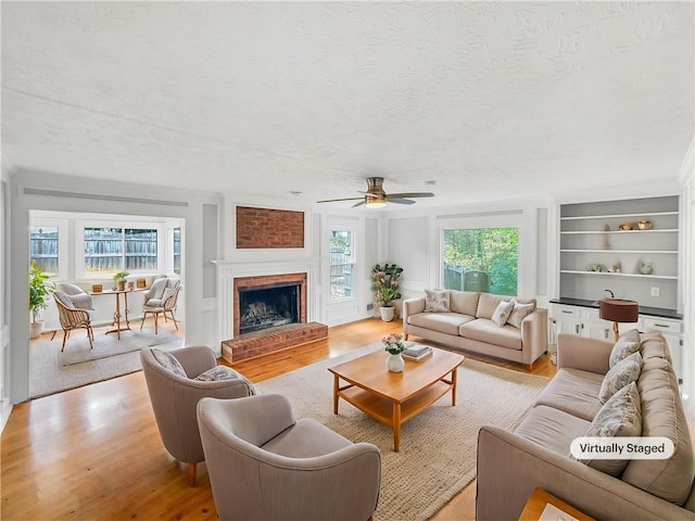 living room featuring a textured ceiling, light hardwood / wood-style floors, a brick fireplace, and a wealth of natural light