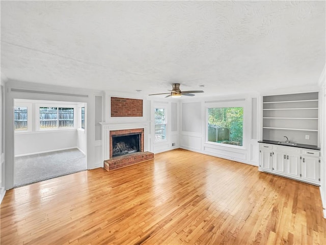 unfurnished living room with a textured ceiling, ceiling fan, light wood-type flooring, and a fireplace