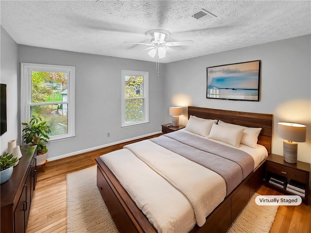 bedroom with multiple windows, light hardwood / wood-style flooring, and a textured ceiling