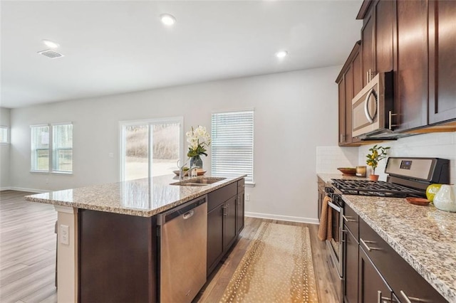 kitchen with light stone counters, a center island with sink, stainless steel appliances, and light hardwood / wood-style floors