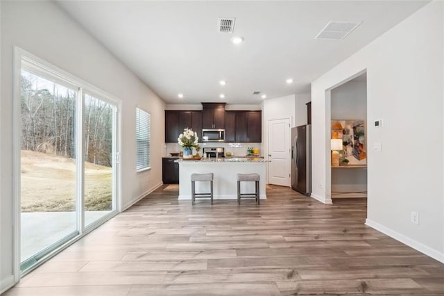 kitchen featuring dark brown cabinetry, stainless steel appliances, a kitchen breakfast bar, a kitchen island with sink, and light wood-type flooring