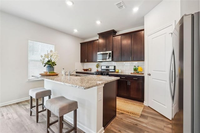 kitchen with light wood-type flooring, stainless steel appliances, a kitchen island with sink, and sink