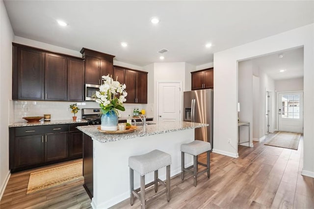 kitchen with a kitchen island with sink, stainless steel appliances, light stone counters, and light hardwood / wood-style floors