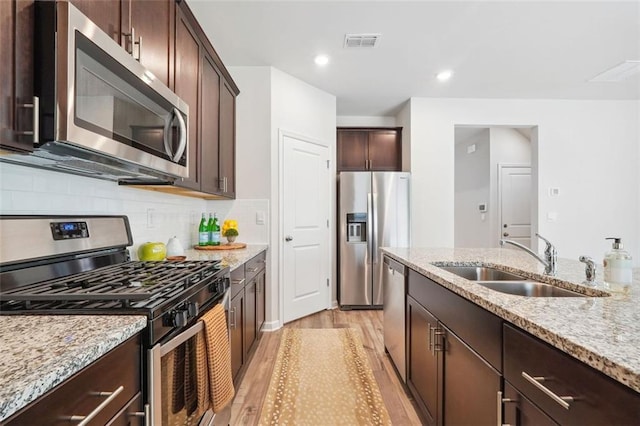 kitchen with decorative backsplash, light stone counters, stainless steel appliances, sink, and light hardwood / wood-style flooring