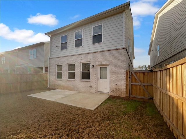 back of house featuring brick siding, a lawn, a fenced backyard, a patio, and a gate