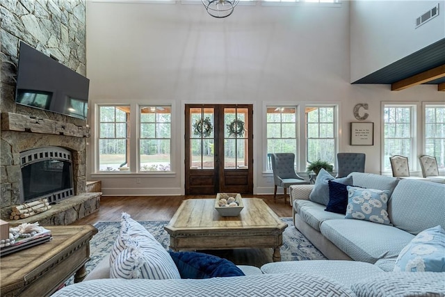 living room with hardwood / wood-style flooring, french doors, a towering ceiling, and a stone fireplace