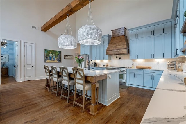 kitchen with premium range hood, a kitchen island with sink, beam ceiling, pendant lighting, and stainless steel range