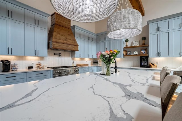 kitchen with custom exhaust hood, tasteful backsplash, hanging light fixtures, light stone counters, and range with two ovens