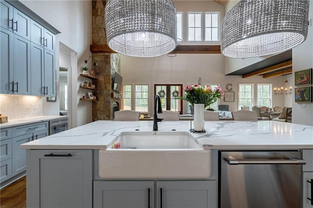 kitchen with stainless steel dishwasher, sink, backsplash, light stone counters, and a notable chandelier