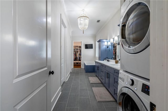 laundry room with dark tile patterned flooring, sink, stacked washer and clothes dryer, ornamental molding, and a notable chandelier