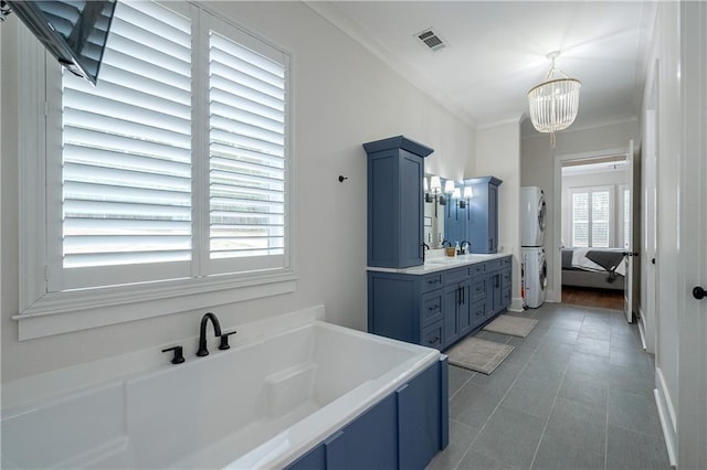 bathroom featuring a chandelier, ornamental molding, vanity, stacked washing maching and dryer, and a bathing tub