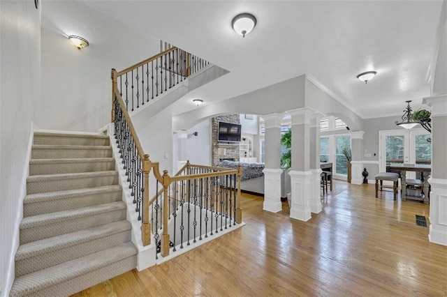 interior space with light hardwood / wood-style floors, ornamental molding, a stone fireplace, and ornate columns