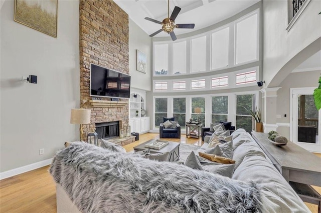 living room featuring ceiling fan, a fireplace, a high ceiling, and light hardwood / wood-style floors