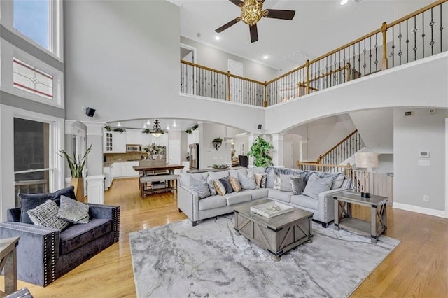 living room with light hardwood / wood-style flooring, ceiling fan with notable chandelier, ornate columns, and a towering ceiling