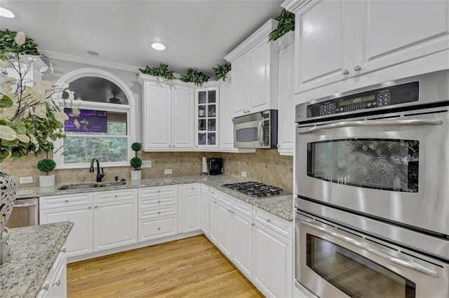 kitchen with light wood-type flooring, light stone counters, stainless steel appliances, backsplash, and sink