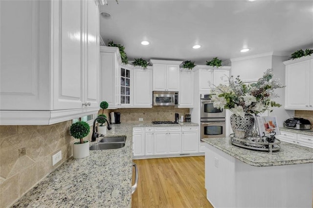 kitchen featuring stainless steel appliances, white cabinets, backsplash, light wood-type flooring, and sink