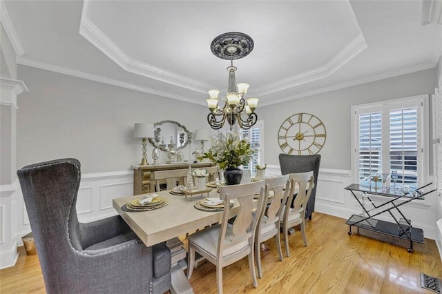 dining area with light hardwood / wood-style flooring, crown molding, a raised ceiling, and a chandelier