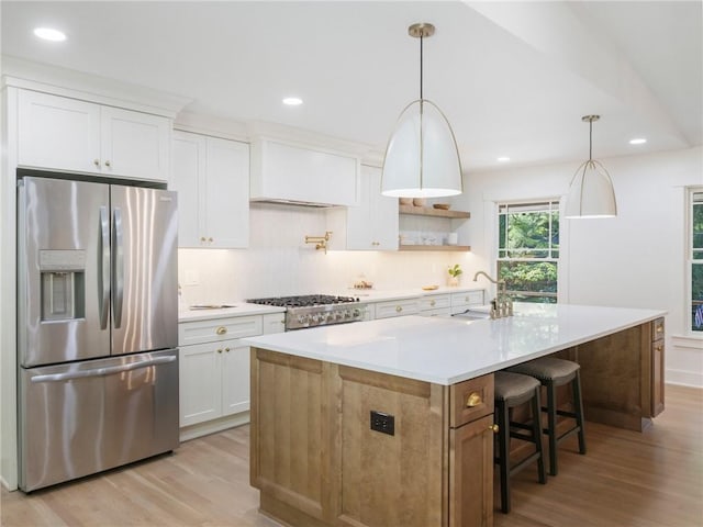 kitchen featuring stainless steel appliances, a center island with sink, decorative light fixtures, light hardwood / wood-style flooring, and white cabinets