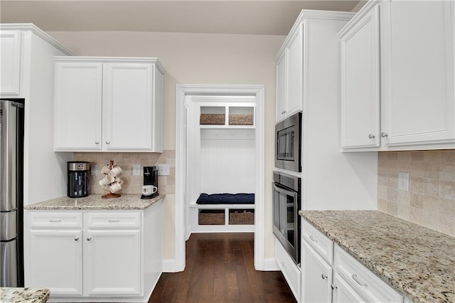 kitchen with appliances with stainless steel finishes, backsplash, dark hardwood / wood-style flooring, white cabinets, and light stone counters