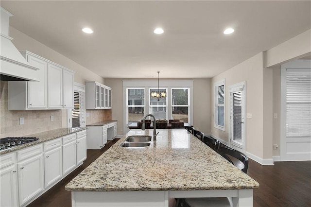 kitchen with white cabinetry, sink, decorative light fixtures, and a kitchen island with sink