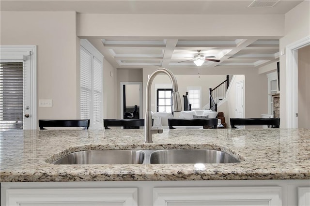 kitchen featuring white cabinetry, coffered ceiling, light stone countertops, and sink