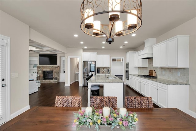 dining room with a stone fireplace, sink, dark hardwood / wood-style flooring, an inviting chandelier, and built in shelves