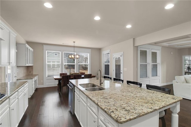 kitchen featuring an island with sink, sink, white cabinets, a kitchen breakfast bar, and hanging light fixtures