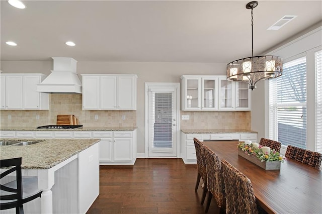 kitchen featuring premium range hood, white cabinetry, hanging light fixtures, light stone countertops, and dark hardwood / wood-style flooring