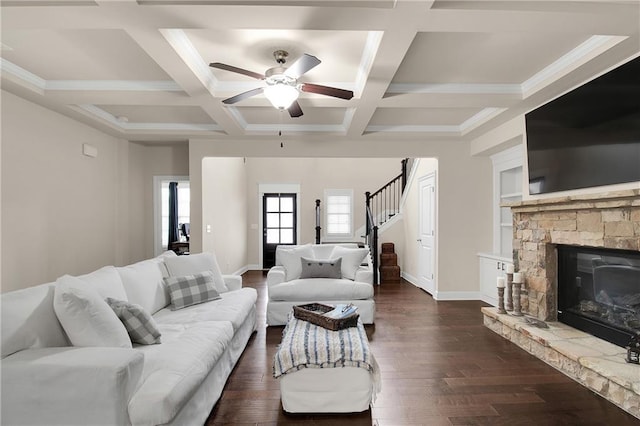 living room featuring coffered ceiling, a stone fireplace, dark hardwood / wood-style flooring, beamed ceiling, and ceiling fan