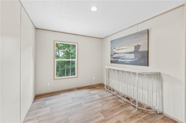 spare room featuring ornamental molding, light hardwood / wood-style floors, and a textured ceiling