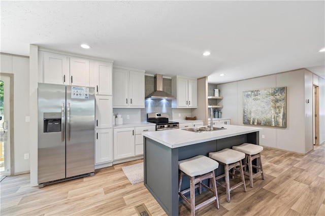 kitchen with wall chimney exhaust hood, white cabinetry, appliances with stainless steel finishes, and a center island with sink