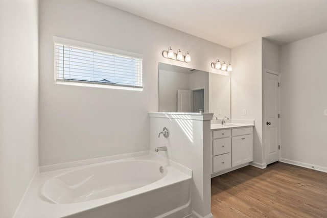 bathroom with wood finished floors, vanity, a bath, and baseboards