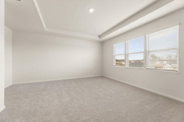 empty room featuring a tray ceiling, carpet flooring, and baseboards