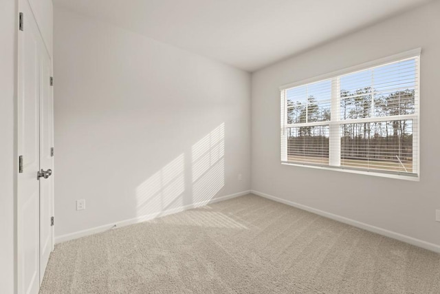 spare room with baseboards and light colored carpet