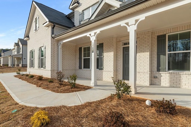 entrance to property featuring a porch and brick siding