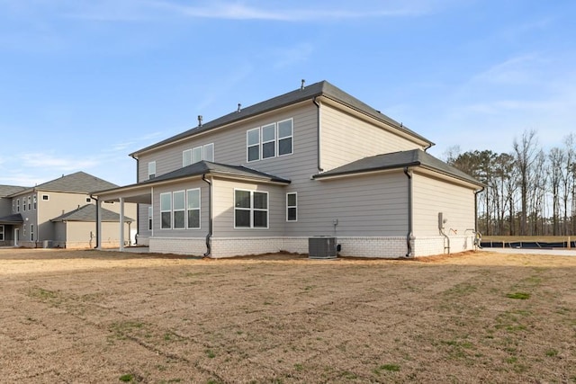 rear view of property featuring central air condition unit and a lawn