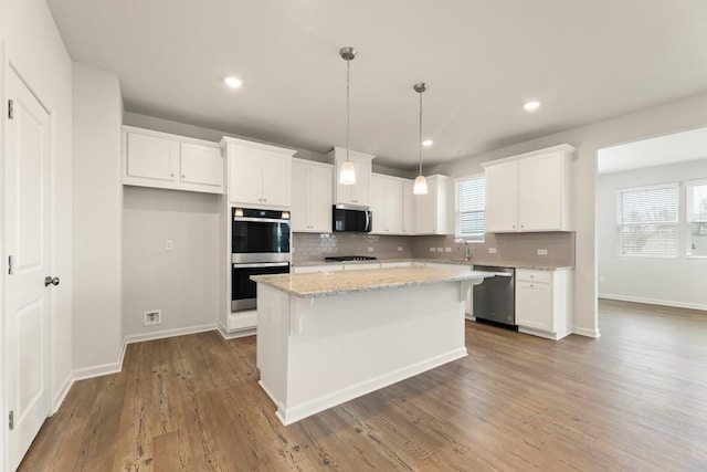 kitchen featuring stainless steel appliances, a center island, white cabinets, and light stone countertops