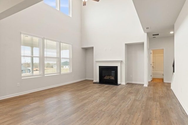 unfurnished living room with light wood finished floors, baseboards, a wealth of natural light, and a glass covered fireplace