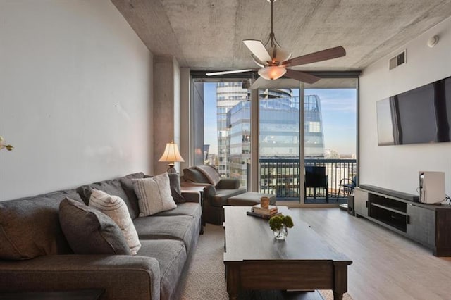 living area featuring light wood-type flooring, a ceiling fan, visible vents, and expansive windows