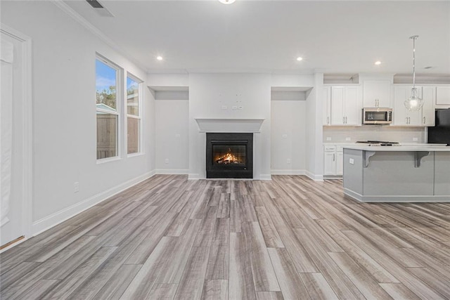 unfurnished living room with visible vents, baseboards, recessed lighting, light wood-style flooring, and a glass covered fireplace