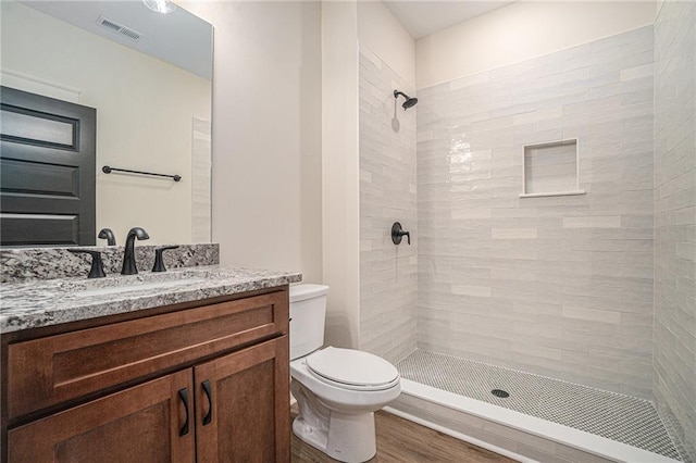 bathroom with hardwood / wood-style flooring, tiled shower, vanity, and toilet