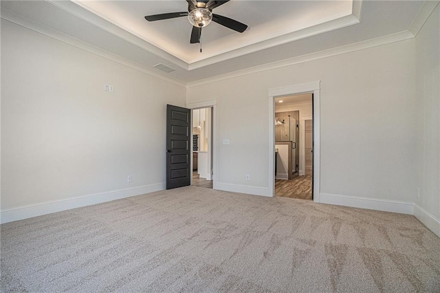 unfurnished bedroom with ornamental molding, light colored carpet, a raised ceiling, and ensuite bathroom