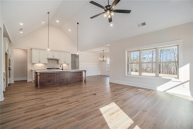 living room with sink, ceiling fan with notable chandelier, wood-type flooring, and high vaulted ceiling