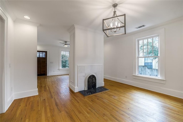 unfurnished living room featuring a tiled fireplace, crown molding, wood-type flooring, and ceiling fan with notable chandelier