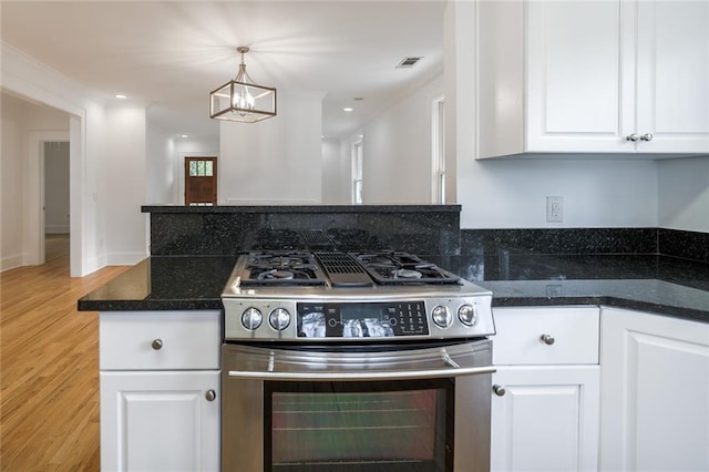 kitchen featuring dark stone counters, pendant lighting, light hardwood / wood-style flooring, stainless steel gas stove, and white cabinetry