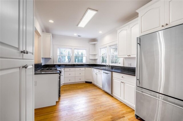 kitchen featuring light wood-type flooring, stainless steel appliances, sink, dark stone countertops, and white cabinetry