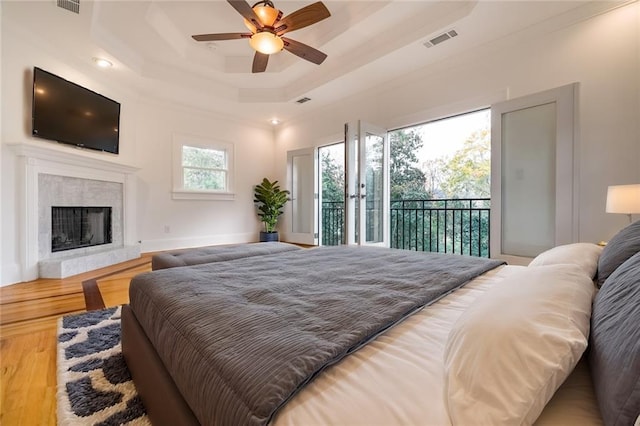 bedroom featuring access to exterior, ceiling fan, a raised ceiling, a premium fireplace, and hardwood / wood-style flooring