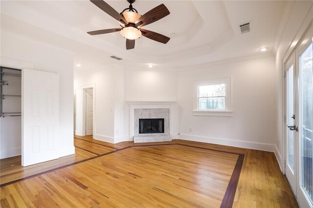 unfurnished living room with a raised ceiling, ceiling fan, light hardwood / wood-style flooring, and crown molding