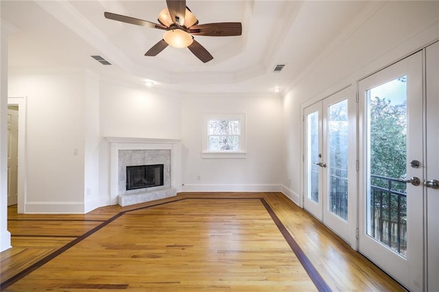 unfurnished living room featuring french doors, a tray ceiling, ceiling fan, crown molding, and light hardwood / wood-style floors